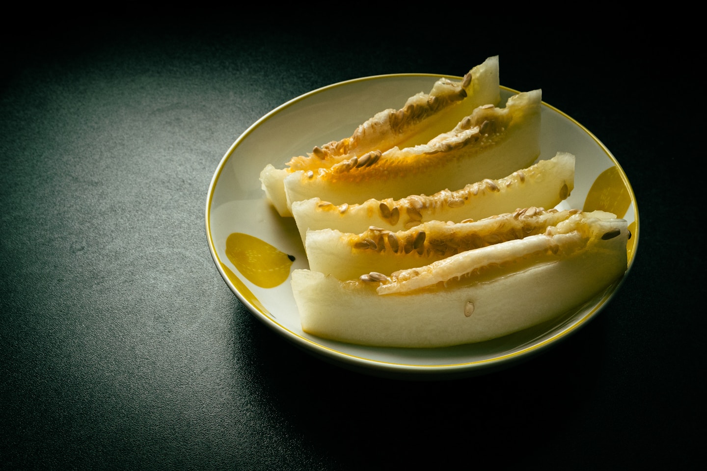 Five melon slices in a white porcelain pasta bowl with some lemon figures on it.